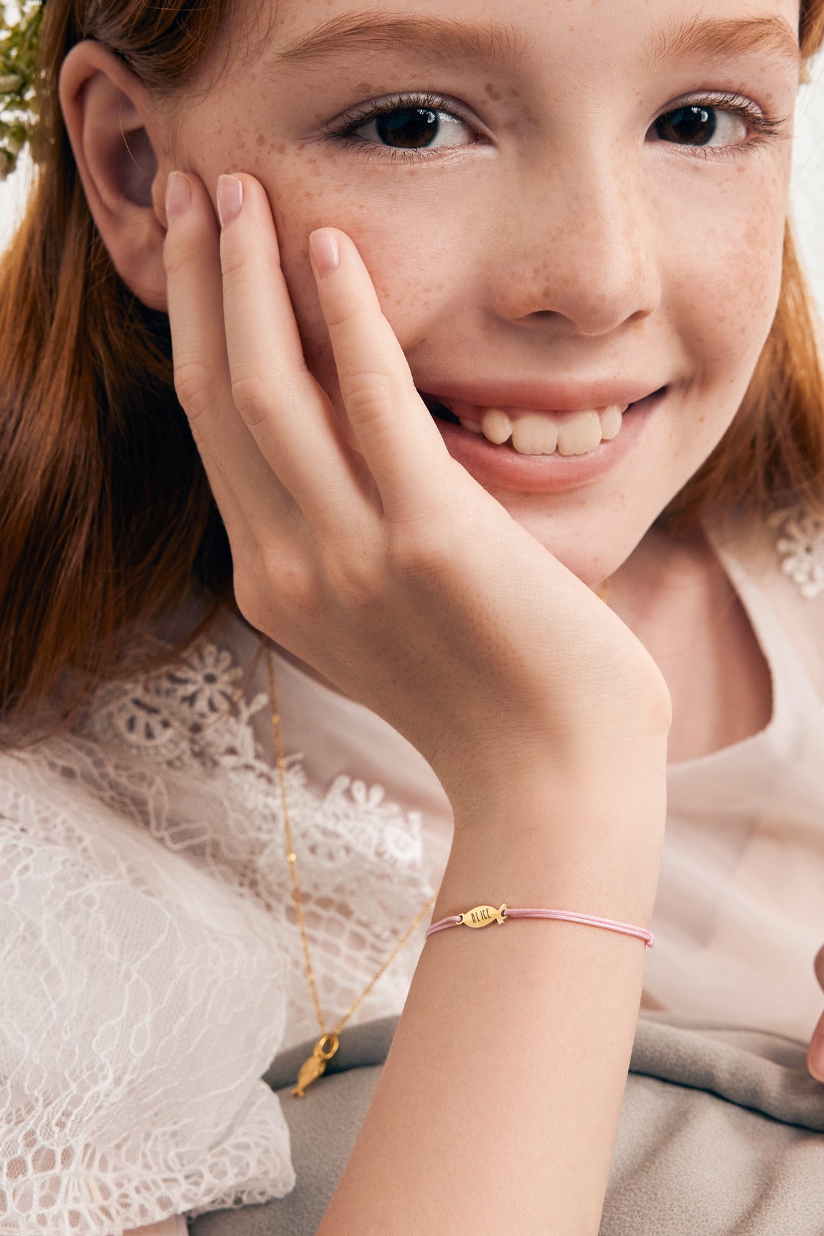 Ichthys Armband mit Gravur in Rosa – Mädchen trägt Armband mit Gravur 'Alice', Hand an der Wange
