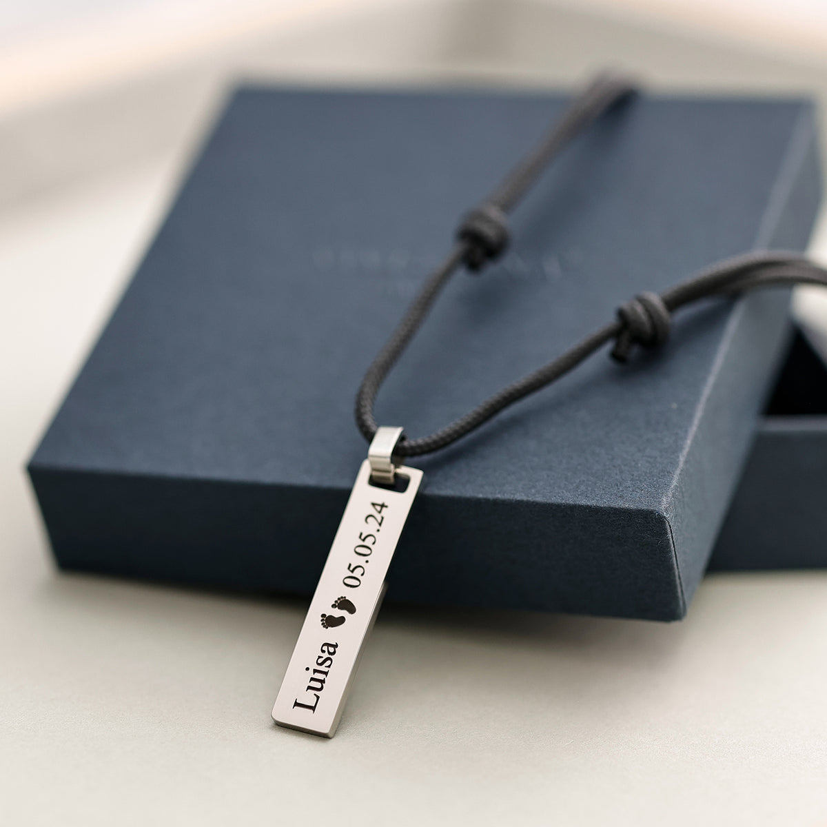 Silberner Stab-Anhänger mit Gravur 'Luisa' und Babyfüßchen-Symbol auf Geschenkverpackung