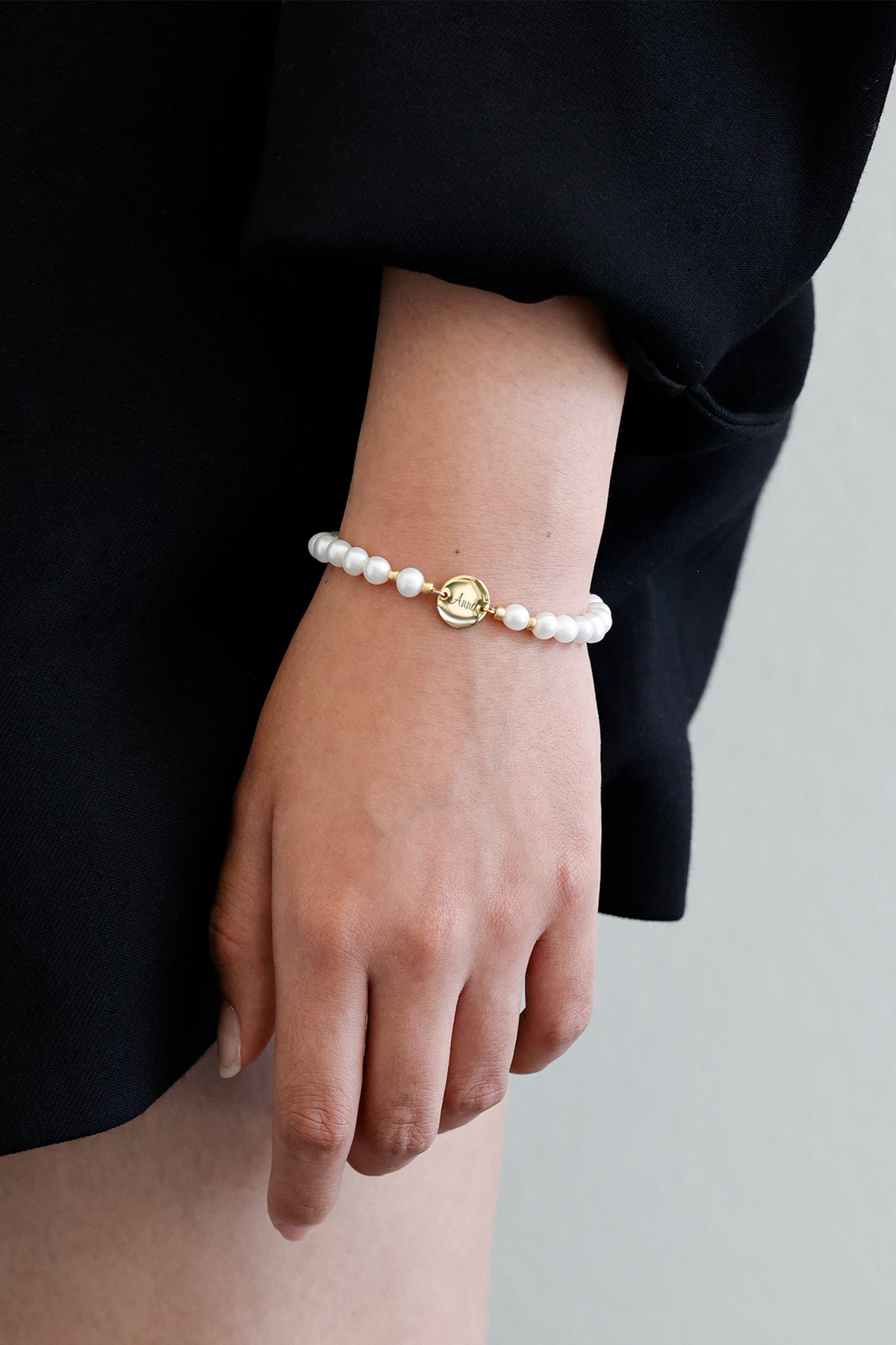 Frau trägt Süßwasserperlen-Armband mit Gravurplättchen 'Anna' vor dunklem Outfit