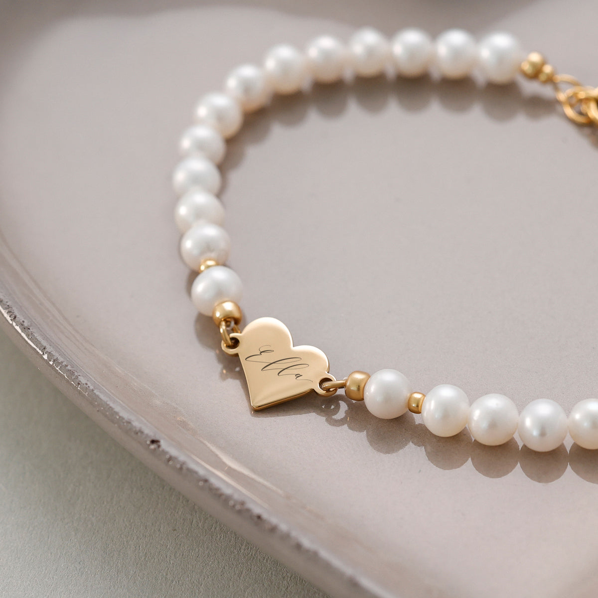 Süßwasserperlen Armband mit Herzanhänger in Gold auf Keramikschale, Herz mit Namen 'Ella' graviert