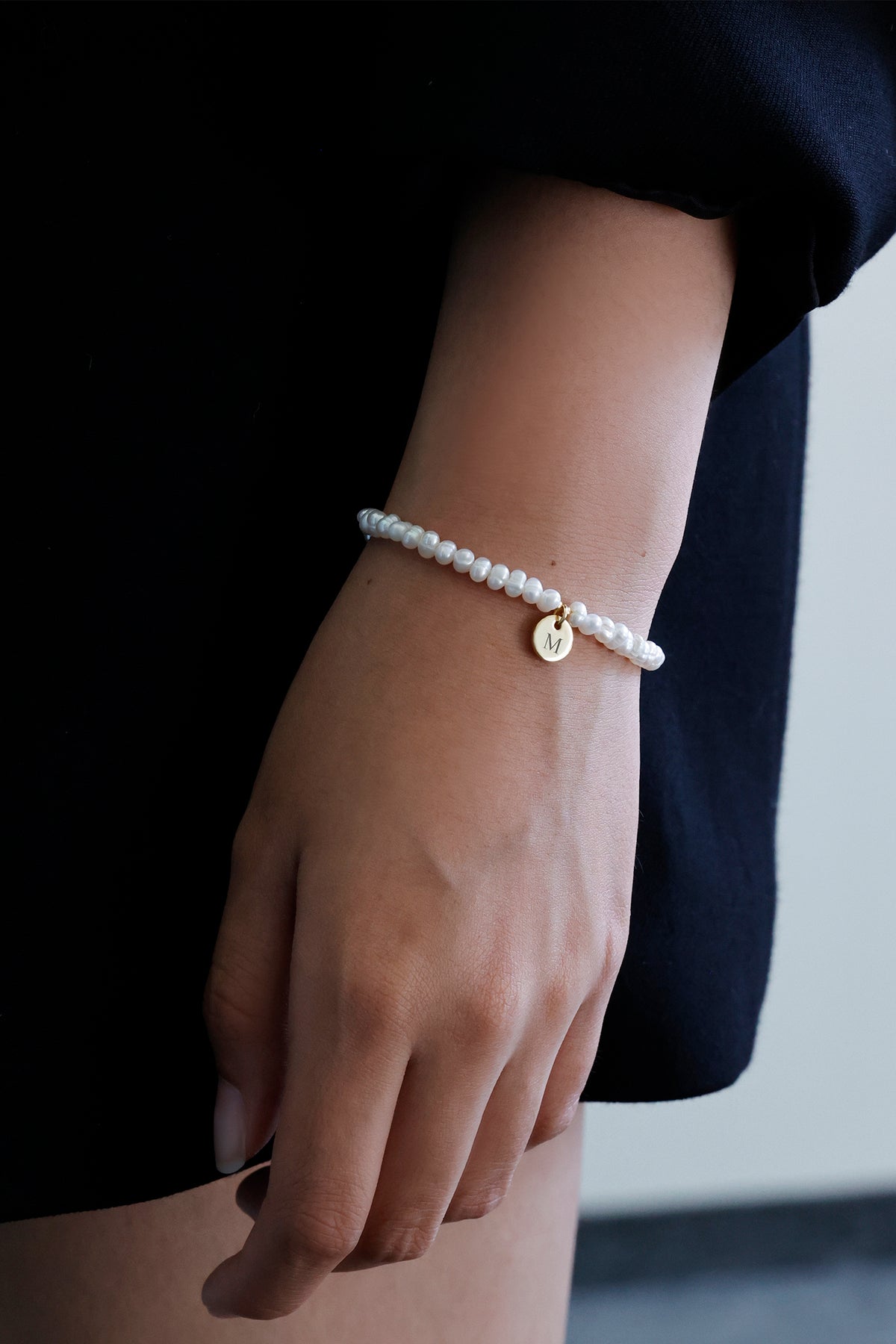 Frau trägt Süßwasserperlen Armband mit goldenem Gravuranhänger seitlich am Handgelenk
