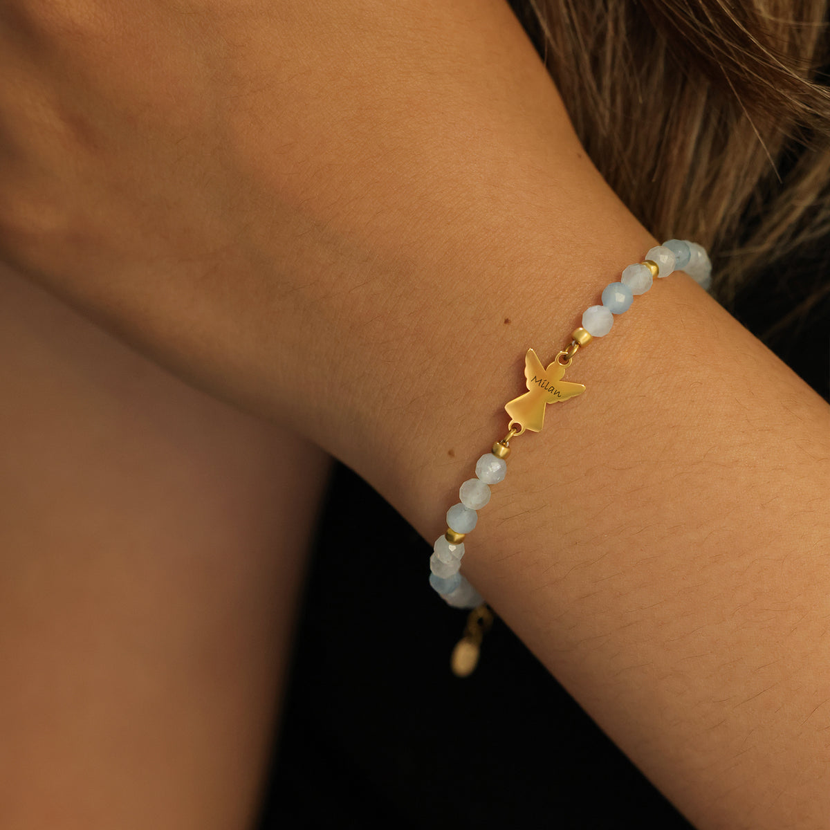 Frau trägt Aquamarin Armband mit goldenem Engelanhänger am Handgelenk