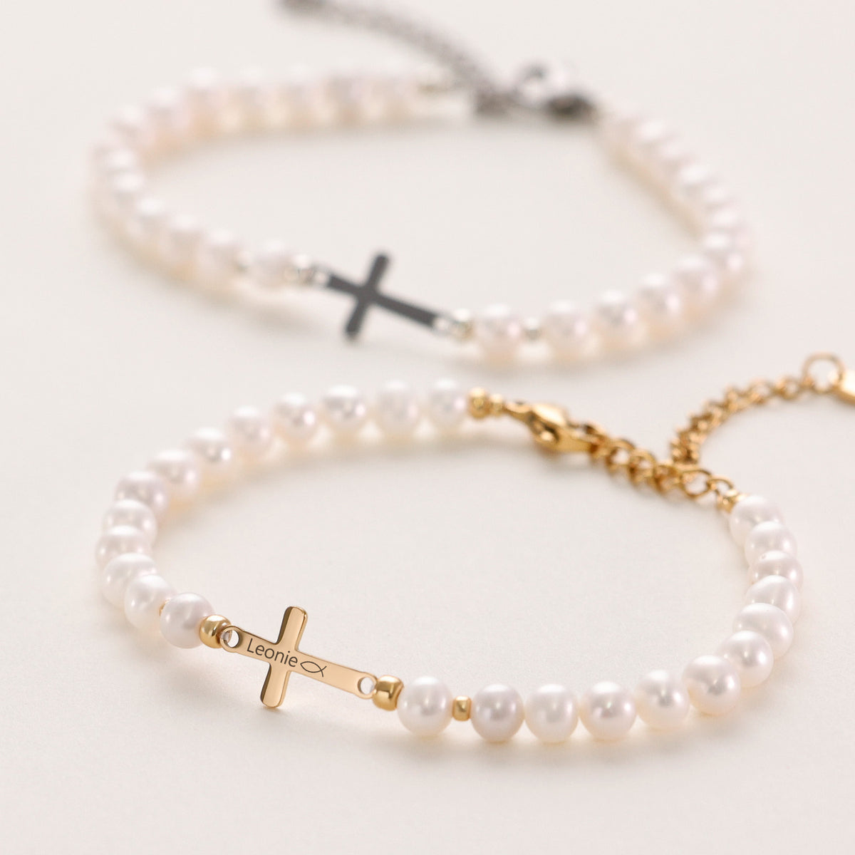 Zwei Armbänder mit Süßwasserperlen im Vergleich – schwarzes Kreuz und goldenes Kreuz mit Gravur 'Leonie'