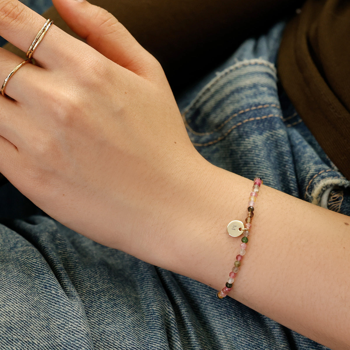 Frau trägt Regenbogen-Turmalin Armband am Handgelenk mit graviertem Plättchen und Initiale