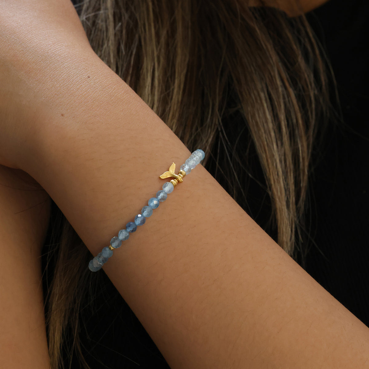Frau trägt Aquamarin Armband mit goldenem Walflosse-Anhänger am Handgelenk