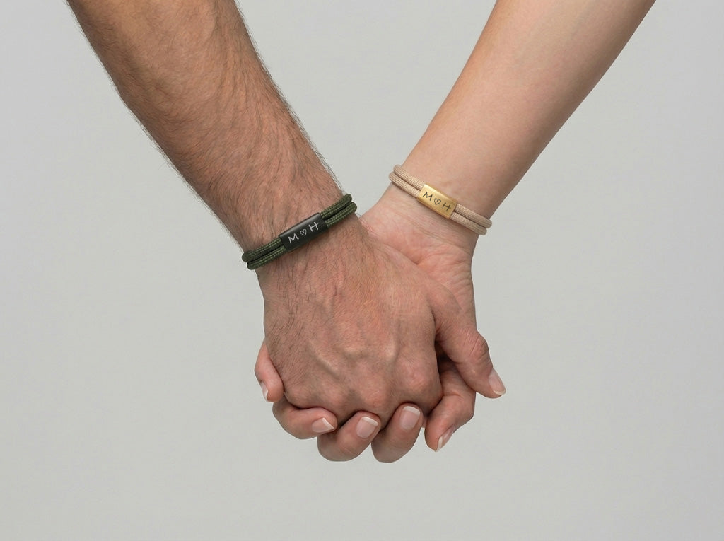 Paar hält Händchen, beide tragen Armbänder mit gravierten Initialen 'M' und 'H'